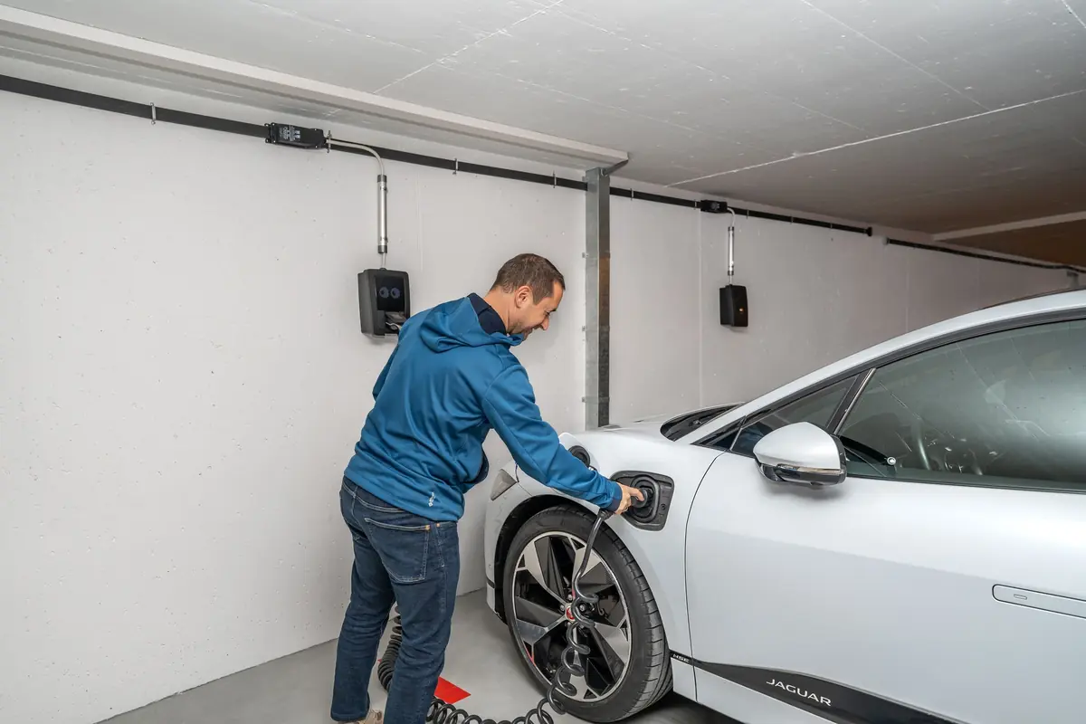 A man plugs his car into a wall charger in a home garage