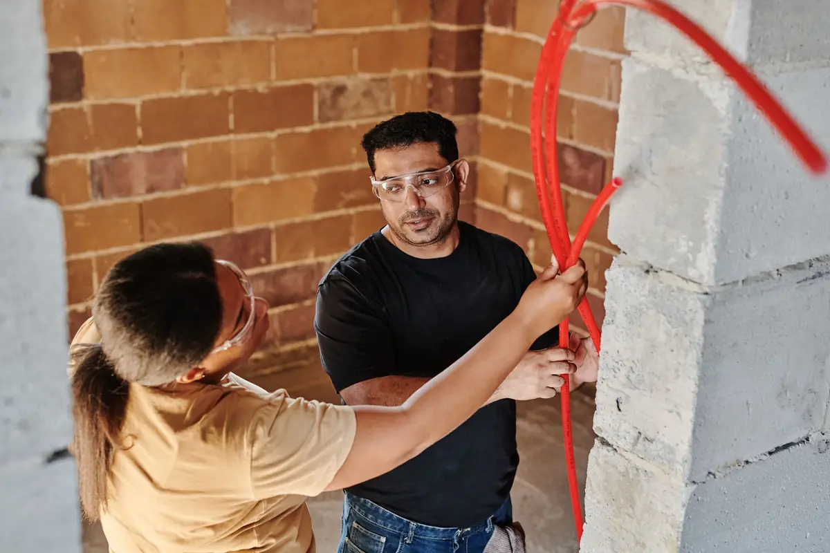 An electrician and a homeowner discuss wiring on a brick wall