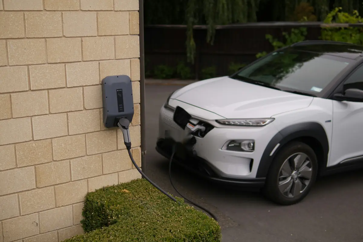 An SUV charging from a wall charger beside its driveway