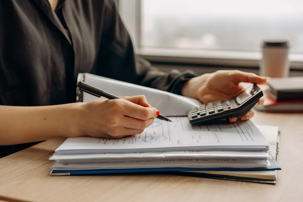 A person works through figures with a calculator and paperwork